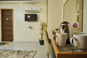A hotel room with a flat-screen TV mounted on the wall, a coffee maker on the counter, and a potted plant. - La Venue Pyramids View Hotel (Giza)