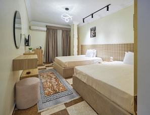 Ein Hotelzimmer mit zwei Betten, einem Schreibtisch, einem Spiegel, einer Deckenleuchte und einem gemusterten Teppich.