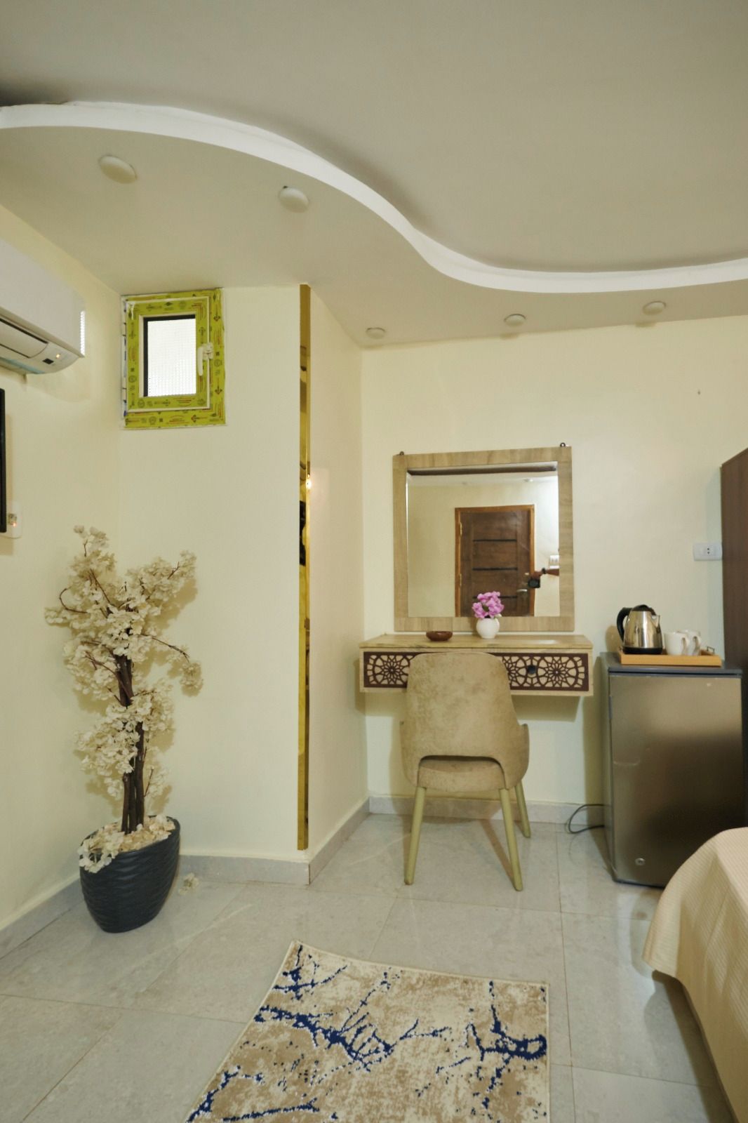 A room with a desk, chair, bed, and a potted plant.