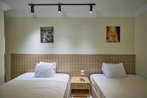 Ein Hotelzimmer mit zwei Betten, einem Holz-Kopfteil, einem Nachttisch mit Fernbedienung und zwei Wandbildern.