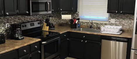 A modern kitchen with black cabinets, stainless steel appliances, a built-in oven, and a dishwasher.