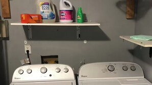 Twee voorladers van Whirlpool met een plank erboven vol met schoonmaakmiddelen.