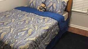 Een bed met een bedsprei met patroon, een teddybeer en een houten hoofdbord.
