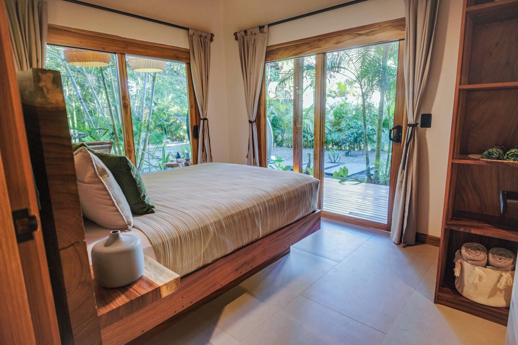 Un dormitorio con una cama grande, cabecera de madera y vistas a un jardín a través de amplios ventanales.