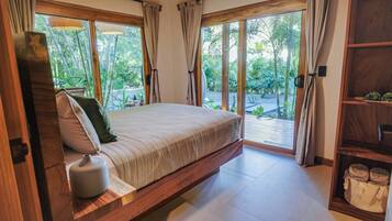 Un dormitorio con una cama grande, cabecera de madera y vistas a un jardín a través de amplios ventanales.