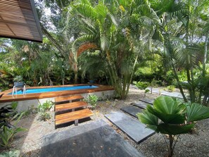 Una piscina rodeada de plantas tropicales y escalones de madera que bajan a ella.