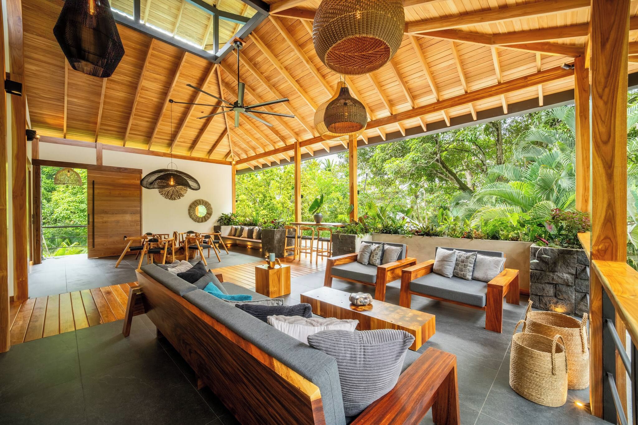 Un espacio interior amplio con techo de madera, un sofá grande y una zona de comedor con sillas.