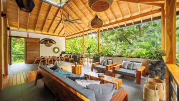 Un espacio interior amplio con techo de madera, un sofá grande y una zona de comedor con sillas.