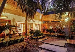 Um jardim interno com teto de madeira, paredes de pedra e diversas plantas.