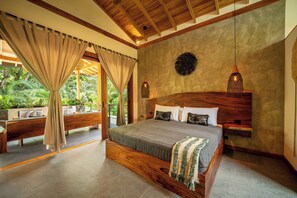 Um quarto espaçoso com uma cama grande, cabeceira de madeira e vista para vegetação exuberante.