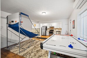 Een kamer met een pooltafel, een klein basketbalmandje en een keuken op de achtergrond.