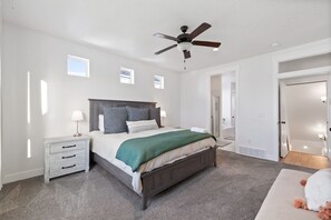 Een slaapkamer met een bed, nachtkastjes, een plafondventilator en een deur naar een andere kamer.
