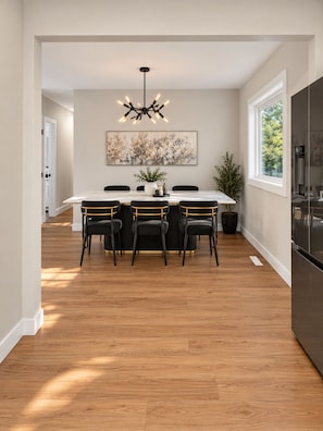 A modern dining area with a marble table, black chairs, a chandelier, and a large window. - Cozy luxurious room with Ensuite washroom in Regina’s best location (Regina)