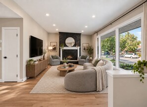 A modern living room with a fireplace, comfortable seating, and a large window offering a view of the outside. - Cozy luxurious room with Ensuite washroom in Regina’s best location (Regina)