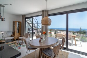 Ein modernes Wohnzimmer mit einem runden Tisch, Stühlen, einer Couch und Meerblick durch große Fenster.