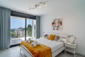 Ein modernes Schlafzimmer mit einem großen Bett, einem Nachttisch, einem Schreibtisch und Blick ins Freie.