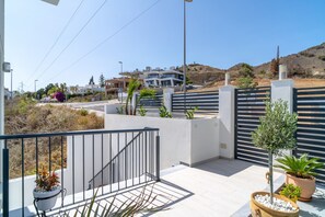 Ein modernes Wohngebiet mit einem verschlossenen Eingang, einer Treppe, die zu einem Balkon führt, und Blick auf einen Hügel mit Gebäuden in der Ferne.