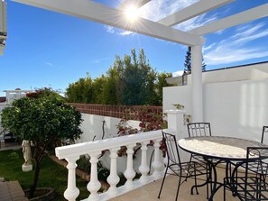 Eine Außenpatio mit weißer Balustrade, einem runden Tisch mit Stühlen und Blick auf Bäume und einen klaren Himmel.