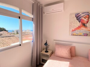 A bedroom with a bed, a nightstand, a lamp, a painting, and a window with curtains. - Apartment in Nerja With Sea Views & Pools (Nerja)