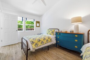 Ett sovrum med en säng, byrå, lampa och ett fönster med utsikt över grönområden.