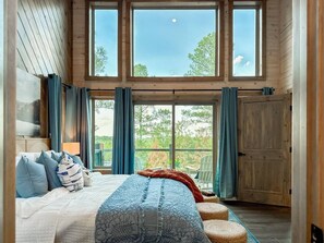 Quarto com cama grande, vista para o exterior e porta deslizante para uma varanda.