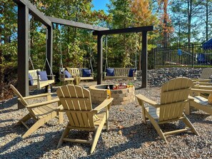 Eine Holzterrasse mit Adirondack-Stühlen, einer Feuerstelle und einem Pergolen-Anbau.