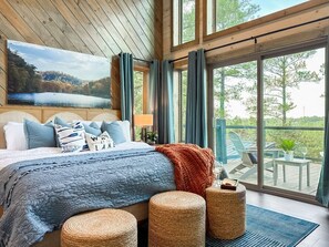Quarto com cama grande, vista para um lago e varanda com mobiliário de exterior.