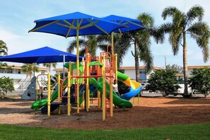 Ein Spielplatz mit Rutschen und Klettergerüsten, umgeben von Palmen und einem klaren Himmel.