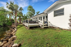 Ein Haus mit einer Terrasse, einem Teich und Palmen.