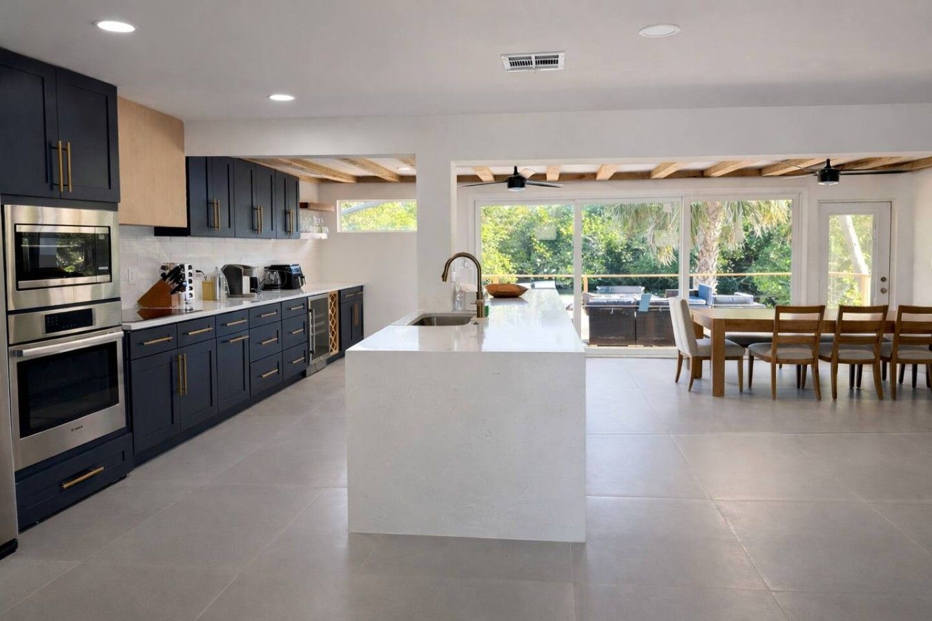 A modern kitchen with built-in appliances, a central island, and a dining area with a view of the outdoors.
