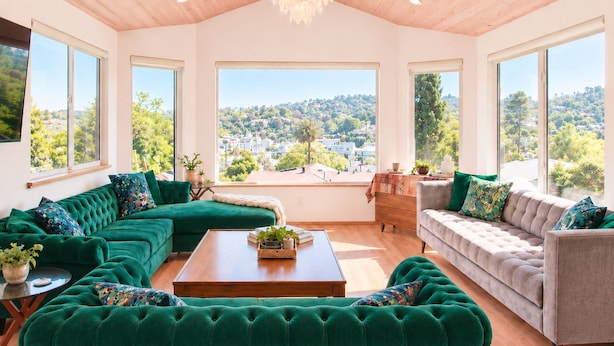 A spacious living room with a large window, a green sofa, a grey sofa, a wooden coffee table, and a chandelier. - 
The Perch  2BR Eagle Rock Home + Views near DTLA (Los Angeles)