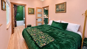 A bedroom with a wooden ceiling, a chandelier, a bed with green bedding, a green floral throw, and a painting on the wall. - 
The Perch  2BR Eagle Rock Home + Views near DTLA (Los Angeles)