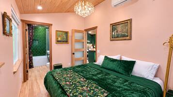 A bedroom with a wooden ceiling, a chandelier, a bed with green bedding, a green floral throw, and a painting on the wall.