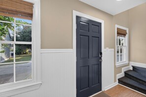 A hallway with a dark door, white trim, and a window with a view of a street and greenery. - Savannah Reserve Savannah Row Suite & Hot Tub (Savannah)