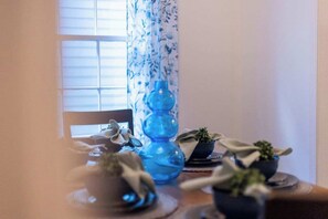 Ein Esstisch mit einer blauen Vase, einem Stuhl und kleinen Topfpflanzen.