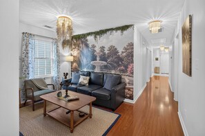 A living room with a dark leather sofa, a wooden coffee table, and a large wall mural of a fountain. - Savannah Reserve Savannah Row Suite & Hot Tub (Savannah)