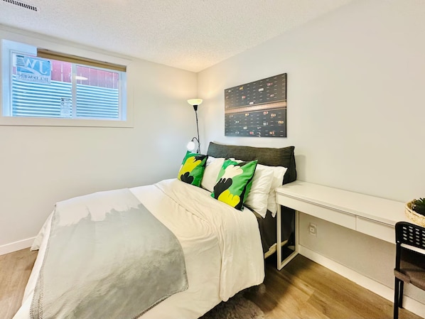 A bedroom with a bed, a desk, and a window.