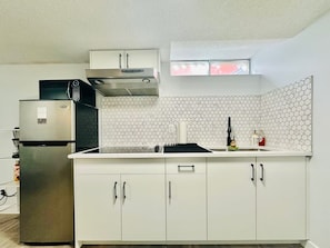 A modern kitchen with a stainless steel refrigerator, a built-in oven, and a microwave. There is a window above the sink, and the backsplash is made of hexagonal tiles.