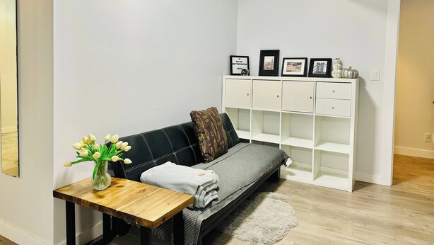 A modern living room with a black sofa, a wooden coffee table, a white cabinet, and a vase of white flowers. - Location! Close to Everything! FREE Banff Pass! (Calgary)