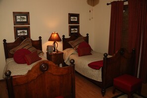 Ein Zimmer mit zwei Holzbetten, jeweils mit Kopfteil, einem Nachttisch mit Lampe und einem kleinen Tisch mit einer Uhr.