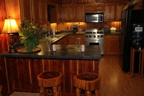 A kitchen with wooden cabinets, a stainless steel stove, a microwave, and a refrigerator. There is a bar area with stools and a lamp. - Best View on the Little Red River, Plus walk-in river access (Heber Springs)