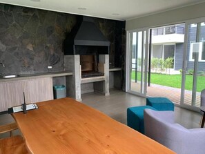 Eine moderne Küche mit einer integrierten Steinwand, einem großen Holztisch und Blick auf einen Garten durch bodentiefe Schiebetüren.