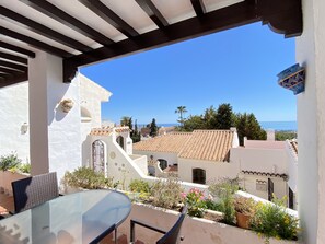 A terrace with a glass table and chairs, overlooking a coastal town with white buildings and a clear blue sky. - Apartment in Nerja With Coastal Views & Pool (Nerja)