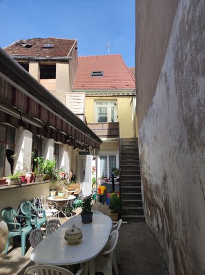 Ein Außenbereich mit einer Terrasse, einem Tisch und Stühlen, umgeben von Topfpflanzen und einer Treppe, die zu einer oberen Ebene führt.