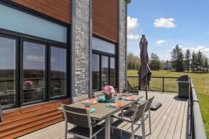 Een terras buiten met een eettafel, grote ramen en uitzicht op het omliggende landschap.