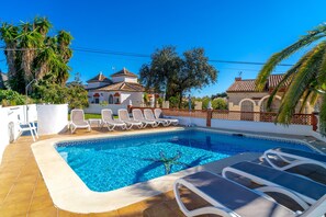 A swimming pool with lounge chairs, surrounded by a white wall and palm trees. - Apartment in Nerja Near the Beach (Nerja)
