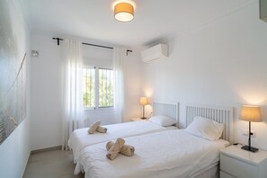 A hotel room with two beds, a window with curtains, an air conditioning unit, and bedside lamps. - Apartment in Nerja Near the Beach (Nerja)