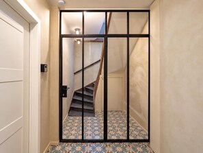 Un couloir avec un sol à motifs, une porte et un escalier doté d’une main courante en bois.