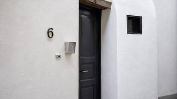 Een witte buitenmuur met een zwarte deur, een klein raam en een bord met het nummer 6.