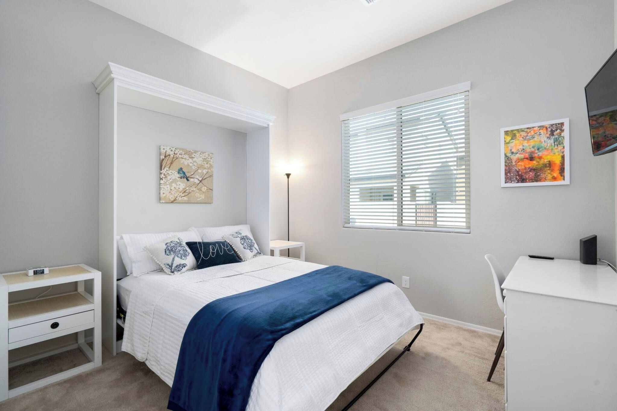 A bedroom with a bed, bedside tables, a desk, and a window with blinds.